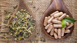 Culture And Swag - a close up of two wooden spoons on a burlap background one containing dried medicinal herbs the other clear capsules of a homeopathic supplement 16X91